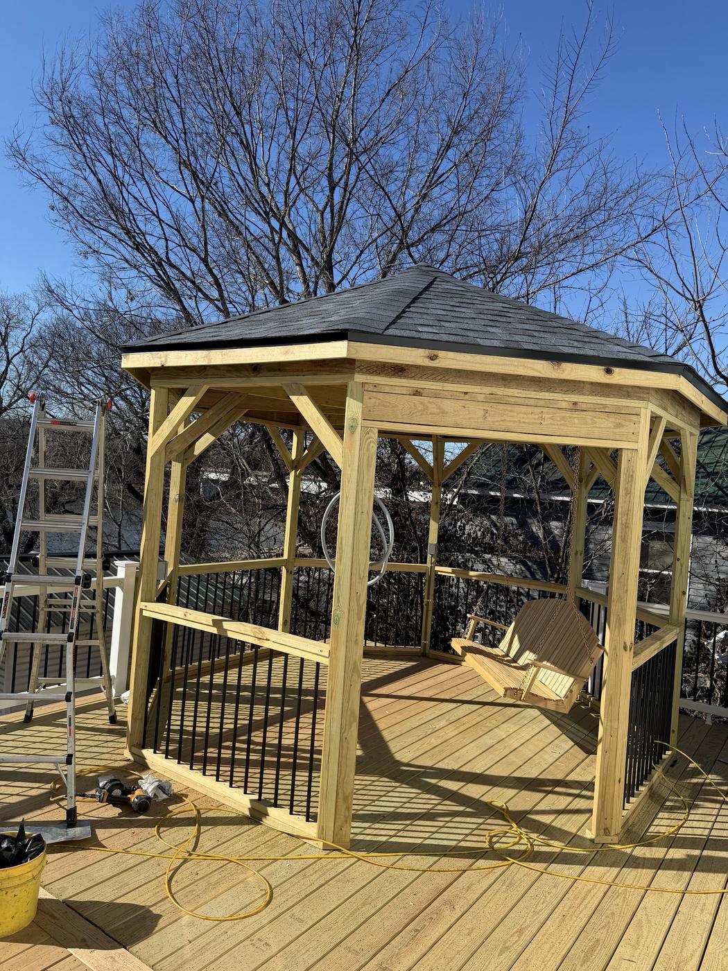 A freshly shingled gazebo roof on a backyard deck, with a porch swing hanging inside